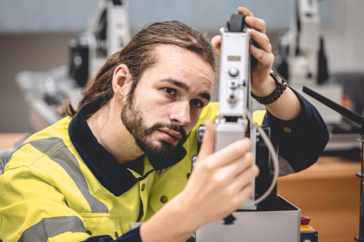 Male aerospace mechanical engineer in a high-visibility jacket focusing intently while adjusting equipment