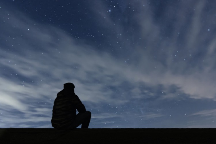 Silhouette of a man sitting and gazing at a star-filled night sky