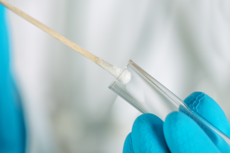 Close-up of a gloved hand holding a DNA swab sample in a test tube, illustrating DNA collection for genetic preservation