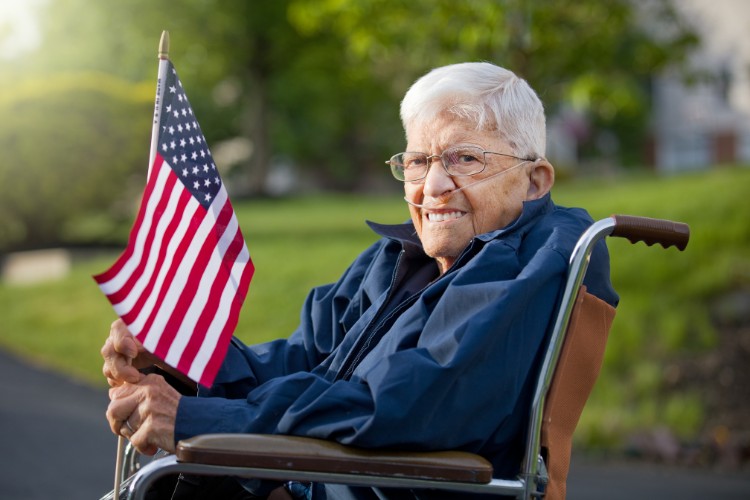 A smiling veteran holding the American flag in a wheelchair, highlighting ways to honor veterans through visits to veterans' homes